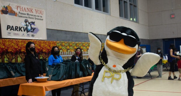Parkway Penguin poses in front of staff at the Newhall Community Center during the Thanksgiving Harvest event.