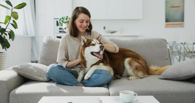 A woman sitting on a couch and petting her dog.