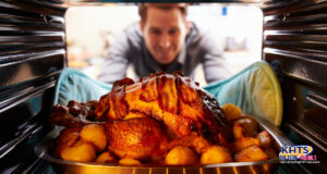 A suspiciously cold-looking roasted turkey topped with bacon strips and surrounded by baked potatoes sits in an oven. A man with oven mitts reaches in to retrieve it from its metal prison.