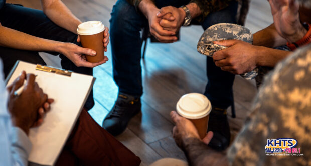 A group of people sitting in a circle drinking coffee, you can only see theri hands and legs. One person holds a clipboard and pen.