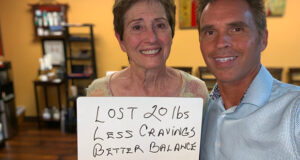 Smiling woman standing next to Sant Clarita Chiropractor Dr Thomas Polucki holding hand written sign that says: “Lost 20 lbs Less Cravings Better Balance”