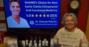 Smiling woman holding hand written sign “Less Pain More Relaxed Better Sleep” at Santa Clarita gentle chiropractic care with Dr. Thomas Polucki DC