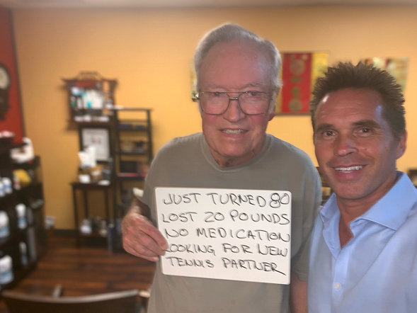 Smiling man holding hand written sign “Just turned 80 Lost 20 pounds No Medication Looking for new tennis partner” at Santa Clarita gentle chiropractic care with Dr. Thomas Polucki DC